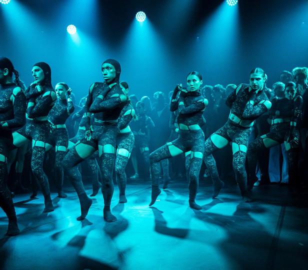 Dancers in lace costumes perform under blue lighting in an immersive dance-rave setting